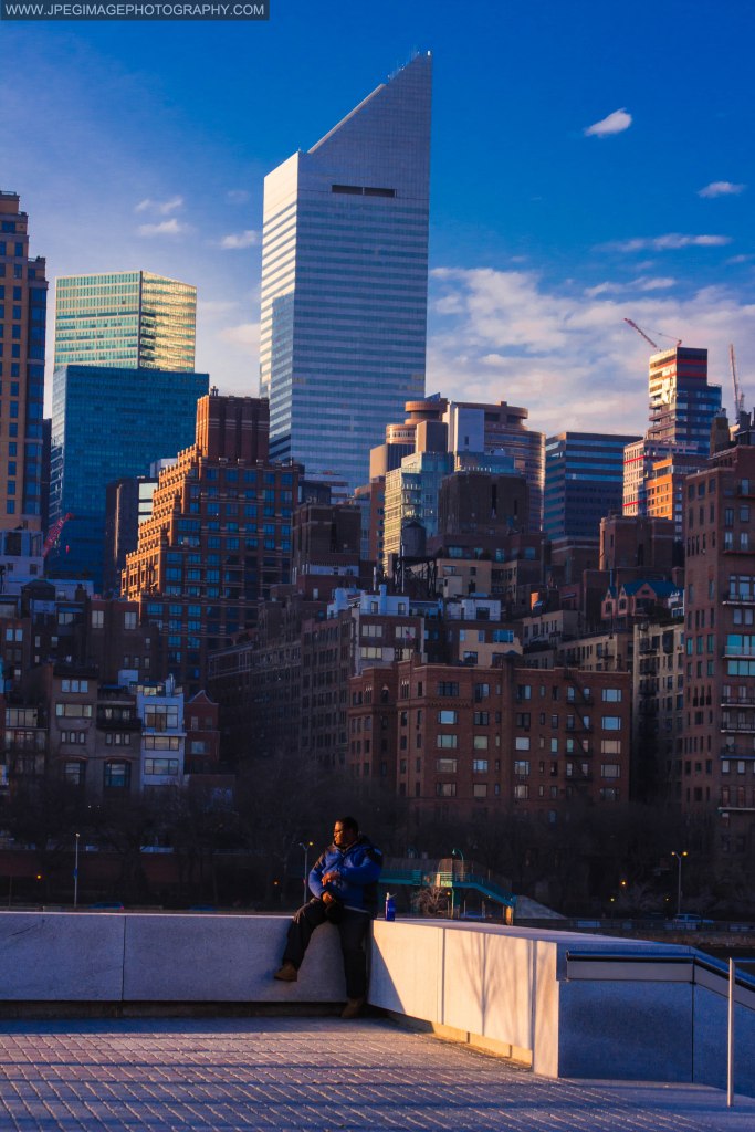 Male individual sitting at Franklin D. Roosevelt Four Freedoms Park plaza, located in Roosevelt Island New York, behind him is the Citigroup Center building in midtown Manhattan. Saturday December 21, 2013.